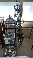Photo shows full view of iron wall sconce, vintage bird cage with missing glass panes, metal lantern partially visible with natural decorative elements inside.