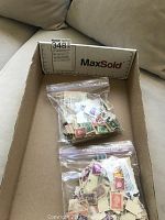 Two transparent resealable plastic bags containing mixed collectible postage stamps from various countries in a cardboard box.