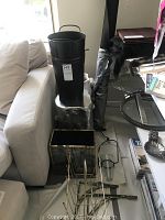 Metallic silver log stool on floor with two black metal containers mounted on top and metal rod elements stacked in front.