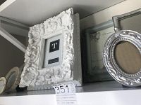 Photo showing ornate white wood frame with floral and leaf motifs, oval metal frame, and smaller round frame.