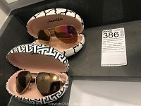 Two pairs of aviator sunglasses with their respective patterned hard cases and a MaxSold tag