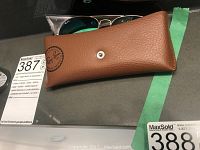 Brown Ray-Ban branded sunglasses case with button snap closure, partially open with sunglasses visible inside