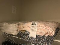 Two stacks of folded blankets and pillow cases on wire shelf, one pile with white pillow cases and two blankets with striped patterns.