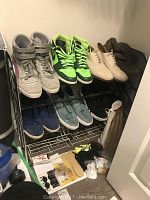 Photo of shoe rack with multiple pairs of men's size 13 shoes including Puma high-tops, Nike Air Jordans, beige dress shoes, and brown leather boots, along with shoe care accessories on the floor.