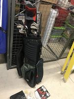 Photo of golf bag standing upright holding irons and clubs, also shows assorted accessories on floor in front