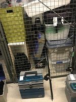 Assembled fishing rod and reel leaning against wire cage next to closed tackle box