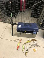 Photo of fishing rod with reel, tackle box, and a selection of large lures laid out on ground