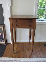 Front view of the wooden side table showing two drawers with round wooden knobs and turned legs.