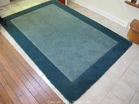Full view of the rectangular dark blue and lighter blue rug placed on a hard floor showing color contrast and condition.