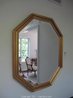 Front view of the octagonal mirror showing the reflective surface and gold frame on a white wall with visible room reflection.