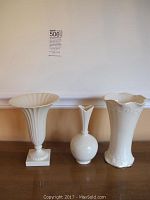 Set of three white vases on wooden table, varying shapes and sizes with floral raised details.