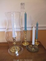 Brass candleholders on a wooden table, one with a glass shield and white candle, others with blue candles