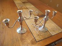 Pair of Gorham sterling silver candelabras photographed on a dining table with floral inlaid tiles, showing full view of both candelabras.
