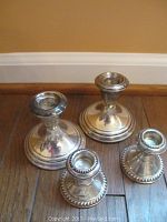 Set of four Gorham sterling silver candlestick holders in two sizes arranged on wooden floor against wall.