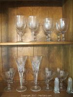 Clear crystal and glass stemware on wooden shelf, showing various wine goblets and Tennessee snifters with salt and pepper shakers.