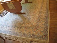 Photo showing the central and border area of the large Oriental area rug under furniture, highlighting colors and wear.