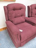 Front angled view of maroon lift chair showing padded tufted backrest, armrest with control remote, fabric upholstery, and nailhead trim detailing