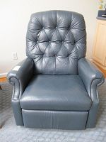 Front view of blue faux leather recliner chair showing tufted backrest, padded arms, and footrest in closed position.