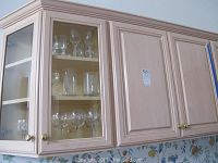 Two kitchen cabinets with clear glassware behind glass and open cabinet doors showing multiple types of glassware.