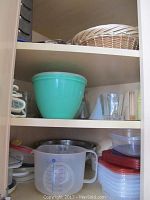 Cabinet with plastic food storage containers including a turquoise large bowl, clear measuring cup, and assorted lids.