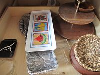 Shows trays including rectangular plastic tray with colorful fruit designs, small black tray, and embossed silver-toned metal trays all arranged in a cardboard box.