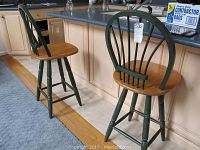 Pair of wooden bar stools positioned near kitchen counter, showing natural wood seats and green painted legs and backrests with wear and chipping paint.