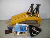Photo showing two yellow plastic car ramps and two black metal jack stands on wooden platform with storage rack holding cleaning and auto care items.
