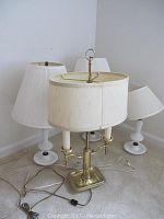 Four lamps grouped together in a corner, showing bases and shades in white and brass.
