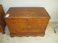 Front view of antique wooden chest showing wood grain with scratches and wear, flat top, keyhole visible on front.