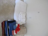 Photo of white quilted comforter, folded beige and blue blankets, and red cloth napkins stacked on carpet