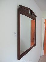 Full frontal view of the tall rectangular wall mirror with a dark wooden frame and ornate carved top, mounted on a wall.