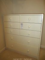 White veneer MDF drawer set with multiple drawers shown from front and side angles in a room corner.