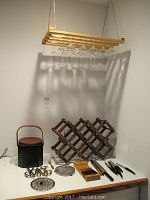 Wooden hanging stemware rack with multiple stemmed glasses, wooden folding wine rack, knives, ice bucket, and two round metal trivets on a counter.