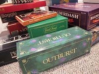 Several board game boxes stacked, showing titles including Outburst, Balderdash, Pictionary, and Boggle.