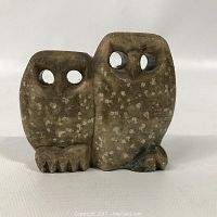Front view of intertwined pair of small carved stone owls showing hollow eyes and spotted patterns