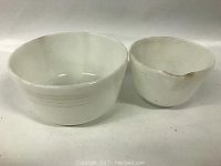 Photo showing two white opaque milk glass mixing bowls: one large and one small with a pour spout, placed side by side on a flat surface.