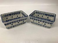 Two square stoneware containers placed side by side displaying their decorating swirl and floral pattern.