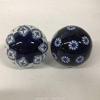 Two blue and white decorative spheres displayed on a white surface, showing their detailed floral and geometric patterns.