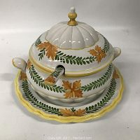 Front angle view of Italian ceramic soup tureen with floral and leaf design, showing lid, handles, spoon, and underplate.