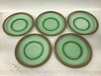 Five green depression glass plates with gilt rim decoration displayed flat on a surface.