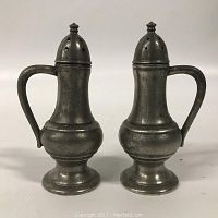Front view of pair of pewter salt and pepper shakers with handles and holes on tops.