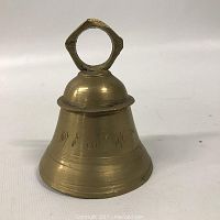 Photo showing the small brass bell about 3.5 inches tall, conical shape, and geometric handle.