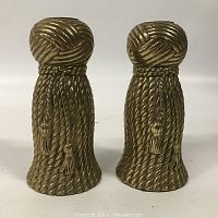 Front view of the pair brass tassel candle holders, showing detailed rope and tassel texture with no candle inserted.