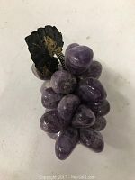 Close-up photo of the polished amethyst grape cluster figurine with metal leaf and stem on a white background.