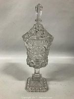 Clear pressed glass candy container with pedestal base and faceted lid photographed against plain background