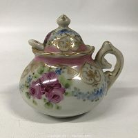 Front view of porcelain mustard pot showing floral design and gilt decoration with lid on.