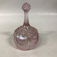 Photo of a cranberry iridescent glass bell with embossed leaf pattern and faceted handle finial against a white background.