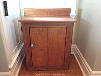 Front view of antique pine washstand showing single door with metal knob and worn wood surface.