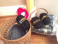 Photo showing multiple black yarn rolls labeled Sultan Luxury Mohair inside and beside a large woven basket, also showing some craft supplies and baskets in the background.