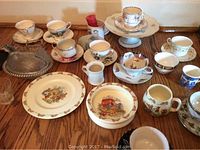 Wide view of entire lot showing Bunnykins plates and bowl, Royal Albert tea cups and saucers arranged on wooden surface.
